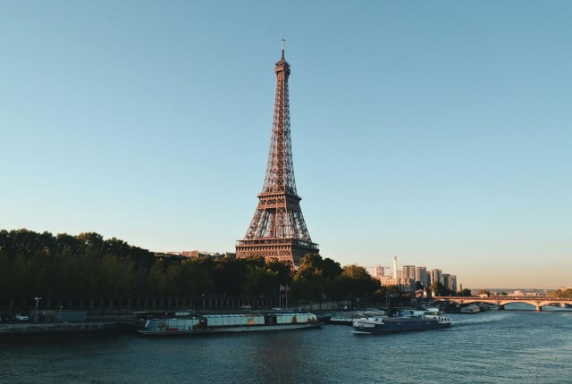 Tour Eiffel en acier ajouré au-dessus de la Seine à Paris, avec bateaux et pont au loin