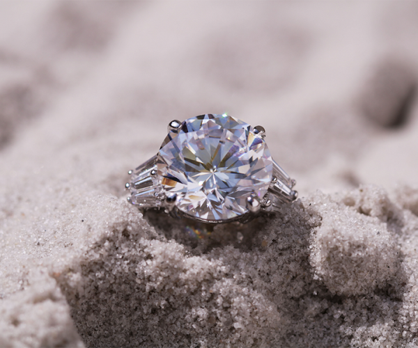a diamond engagement ring laying naked to the eye in the sand on the beach, probably due to someone not being careful enough