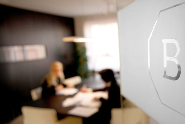 Logo BAUNAT inciso su vetro satinato, sfondo sfocato di consulenza virtuale in showroom