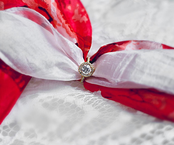 Una fede nuziale appoggiata su un nastro rosso e bianco, che rappresenta il legame d'amore e la promessa di un impegno eterno.