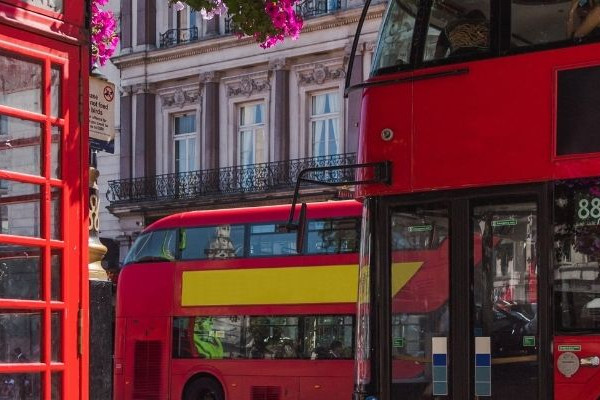 Una fotografia panoramica di una strada di Londra con l'iconica cabina telefonica rossa e gli autobus turistici rossi che ritraggono l'ora di punta della giornata.