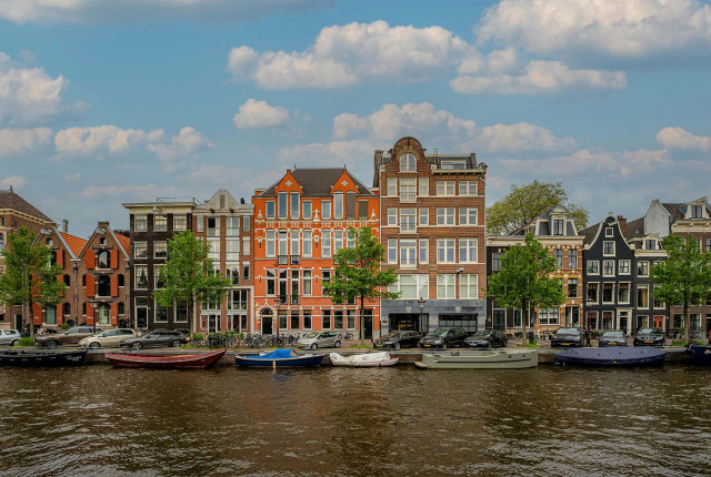 Vista del canale di Amsterdam con case storiche colorate e barche ormeggiate lungo la riva