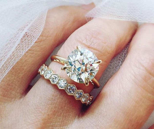 手元に重ね着けされたゴールドの婚約指輪と、六角形モチーフのダイヤモンドエタニティリング