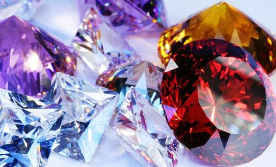 보라, 투명, 빨강, 노랑 등 다양한 색상의 컷팅된 보석 원석과 크리스털이 빛을 반사하며 겹쳐진 클로즈업 이미지