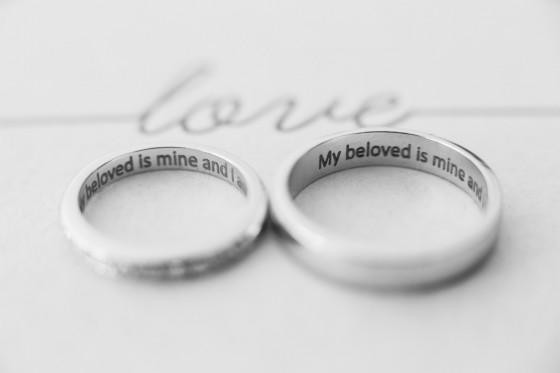 흰색 배경 위에 ‘My beloved is mine and I am his’ 문구가 새겨진 매끈한 화이트 골드 결혼반지 두 개가 나란히 놓인 모습