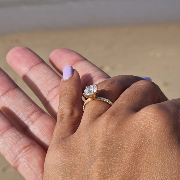 Yellow gold engagement ring with round diamond solitaire and pavé diamond band on a hand