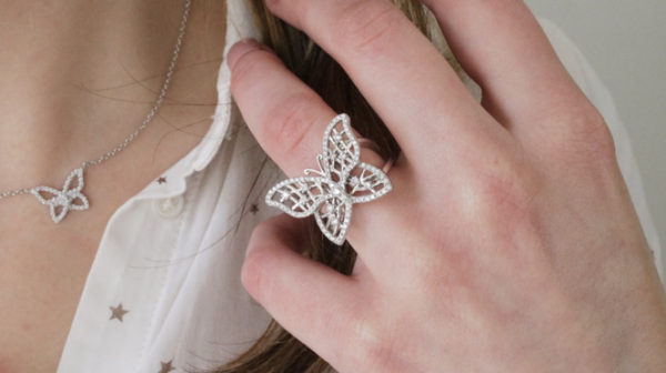 Eine Nahaufnahme eines diamantenen Schmetterlingsrings an der Hand einer jungen Frau. Außerdem trägt sie eine winzige Diamant-Schmetterlingskette.