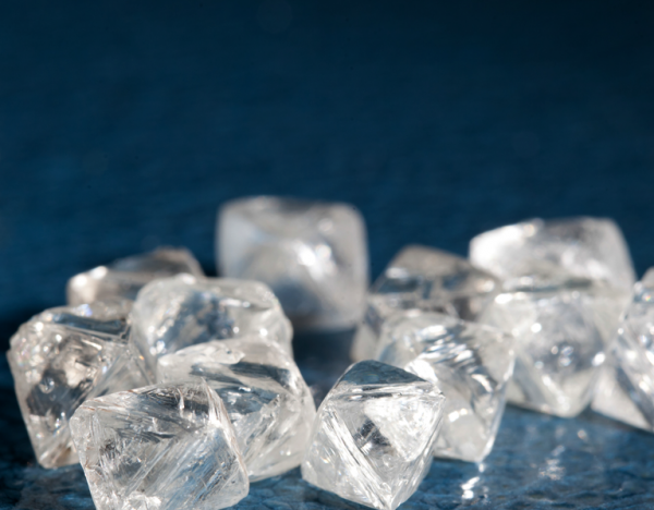 Diamantes en bruto transparentes sobre fondo azul, con facetas naturales y brillo cristalino