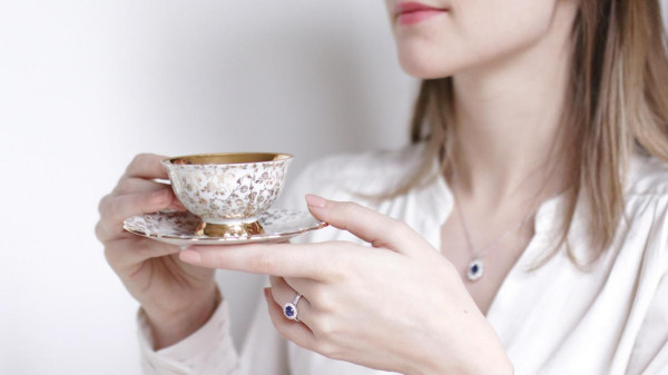 Mujer bebiendo té y usando un anillo de zafiro, una excelente alternativa a los diamantes azules - BAUNAT