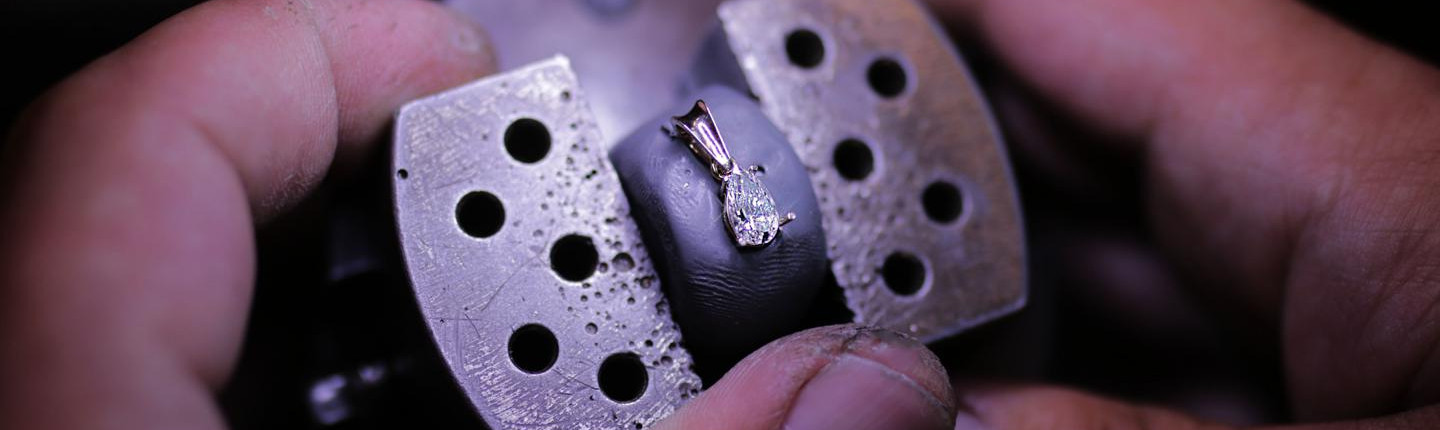 珠宝工匠用金属夹具固定一枚白金梨形钻石吊坠，正在进行个性化定制镶嵌加工