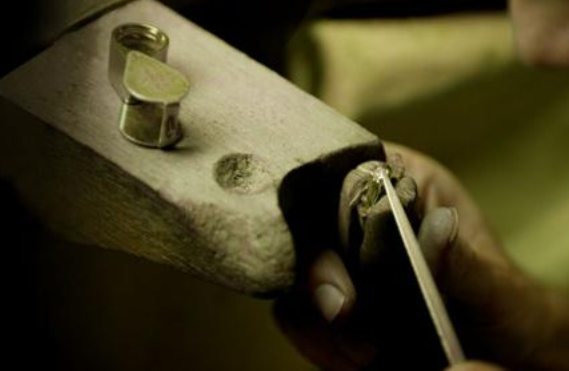 Artisan bijoutier façonnant une bague de fiançailles en or blanc avec diamant sur l’établi.