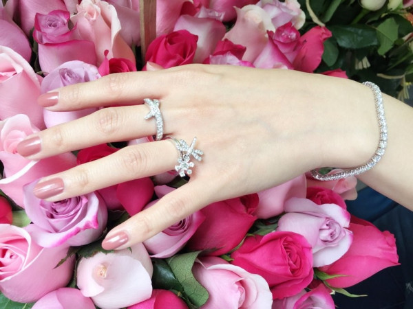Mano con anillos de diamantes y pulsera de oro blanco sobre rosas rosas y fucsias