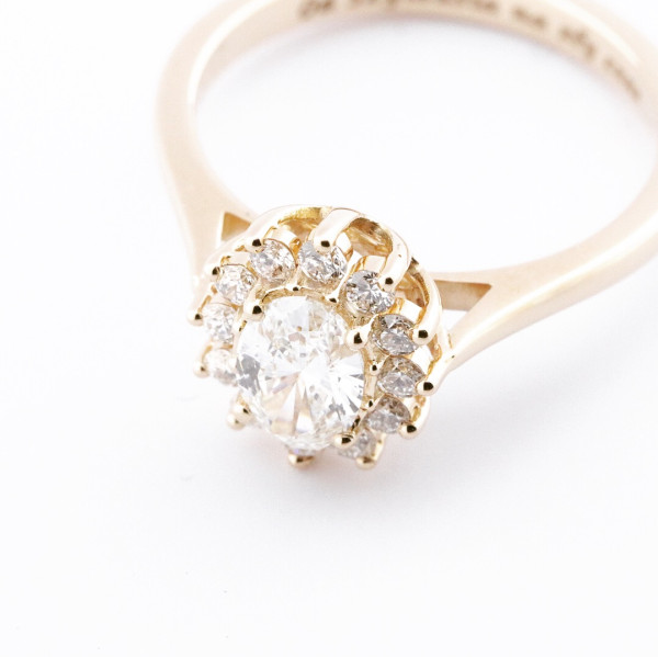Anillo de compromiso en oro amarillo con diamante central oval y halo de pequeños diamantes