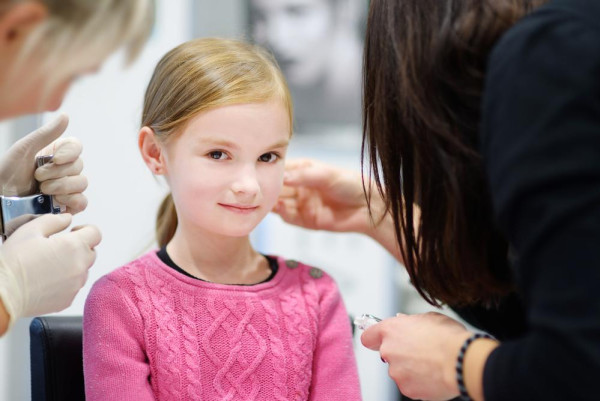 Niña perforándose las orejas en la joyería y recibiendo su primer par de pendientes. - BAUNAT