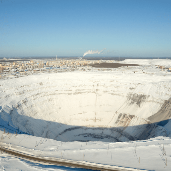 Großer offener Diamanten-Tagebau im Schnee mit tiefem Abbaukrater und Stadt im Hintergrund