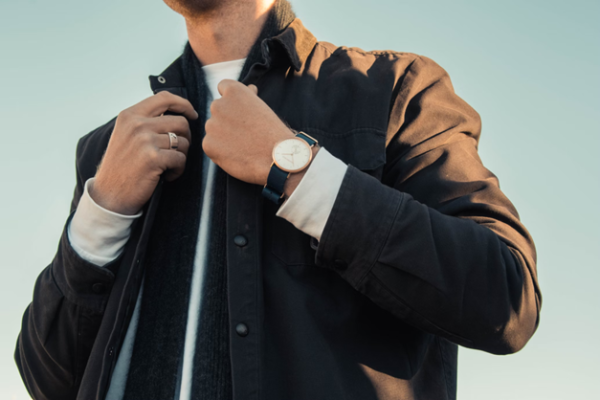 Mann, der selbstbewusst einen schlichten Verlobungsring aus Platin zusammen mit einer Uhr mit Lederarmband trägt