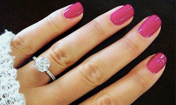 Verlovingsring van witgoud met ronde solitaire diamant in pootzetting op vrouwelijke hand met roze nagellak