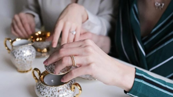 two women holding tea cups and saucers, one wearing a fine engagement ring stacked together with another one, creating a beautiful alliance