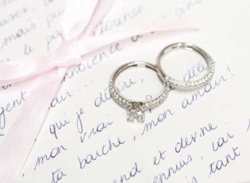 alliance et bague de fiançailles reposant sur une lettre, joliment nouée avec un ruban rose, symbolisant l'amour et l'engagement.