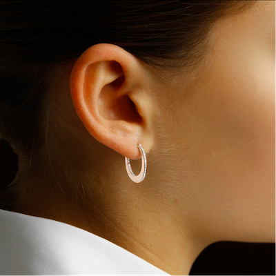 Une femme présente d'élégantes boucles d'oreilles créoles en diamants, rehaussant son apparence et son style sophistiqués.