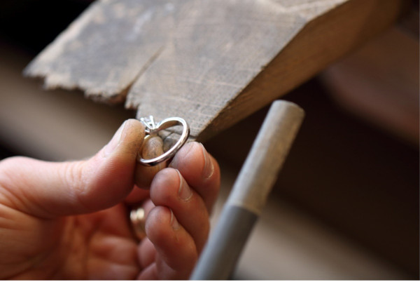 een juwelier werkt met een gereedschap op een machine, gericht op het aanpassen van de maat van de metalen band van een ring