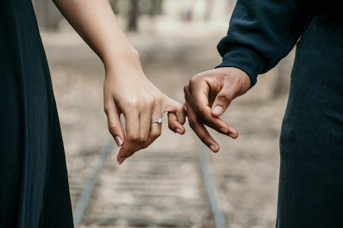 une femme et un homme se tenant par la main et portant d'élégantes bagues de fiançailles