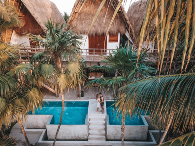 Un couple se tient au bord d'une piscine, encadrée de palmiers luxuriants, profitant d'une journée ensoleillée dans un paradis tropical 