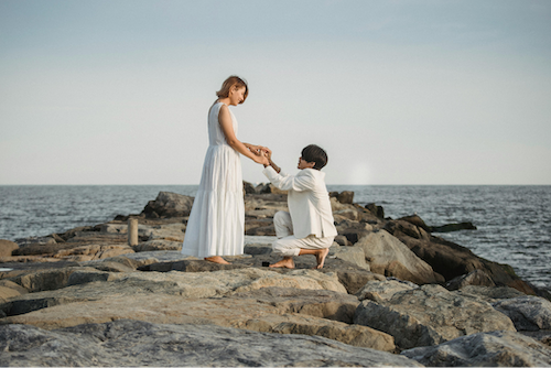 ein Mann, der am Strand für seine Verlobte das Knie beugt und sie bittet, zu heiraten