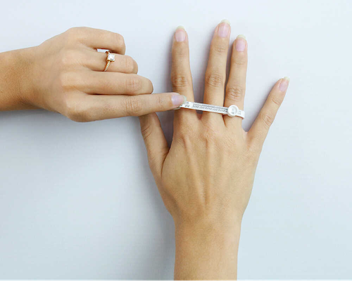 De hand van een vrouw houdt elegant een diamanten ring vast en toont de schittering ervan naast een ringmeter voor een nauwkeurige pasvorm