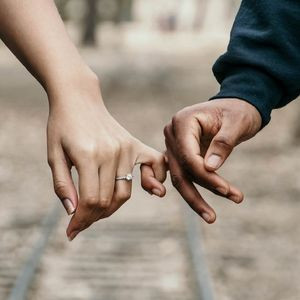 Primo piano di un uomo e una donna che si tengono per mano. La donna indossa un semplice anello di fidanzamento con diamante.