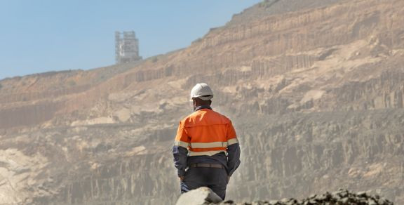 Operaio con casco e giubbotto arancione davanti a una miniera di diamanti a cielo aperto