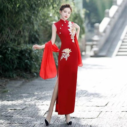 Una donna in qipao rosso con ricami floreali posa elegantemente per una fotografia, mostrando l'abito tradizionale cinese.