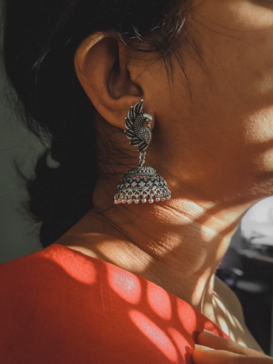A woman in a vibrant red dress, adorned with earrings, showcasing cultural elegance with traditional jewellery of india