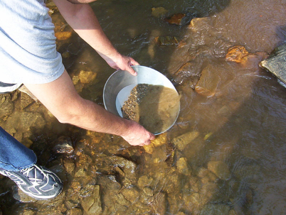 Een man gebruikt een metalen kom in het water en past de goudzoekmethode toe om kostbare goudklompjes te vinden. - Een man gebruikt een metalen kom in het water en past de goudzoekmethode toe om kostbare goudklompjes te vinden.