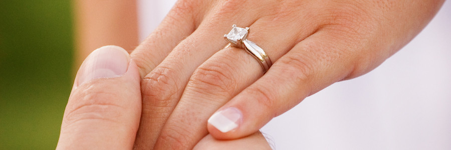 Man grabs hand of woman with diamond engagement ring - BAUNAT