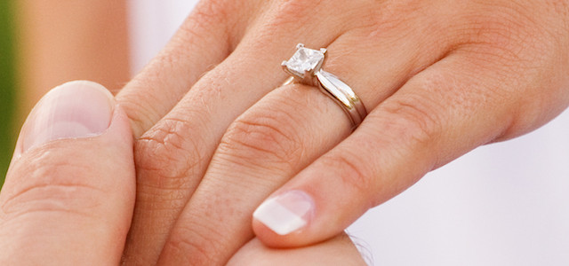 Man grabs hand of woman with diamond engagement ring - BAUNAT