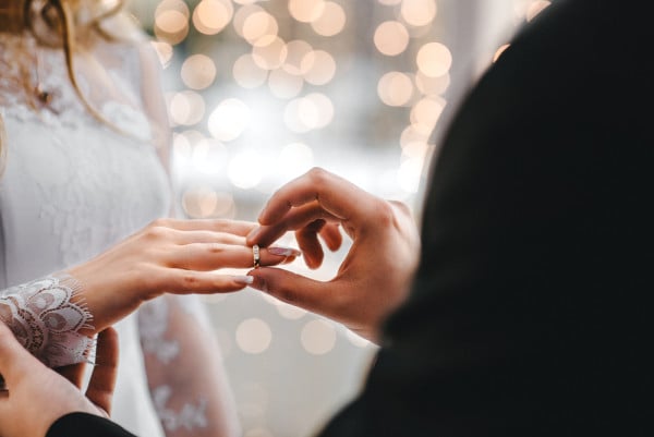groom in christian tradition shoving the bride’s diamond wedding ring on her right hand