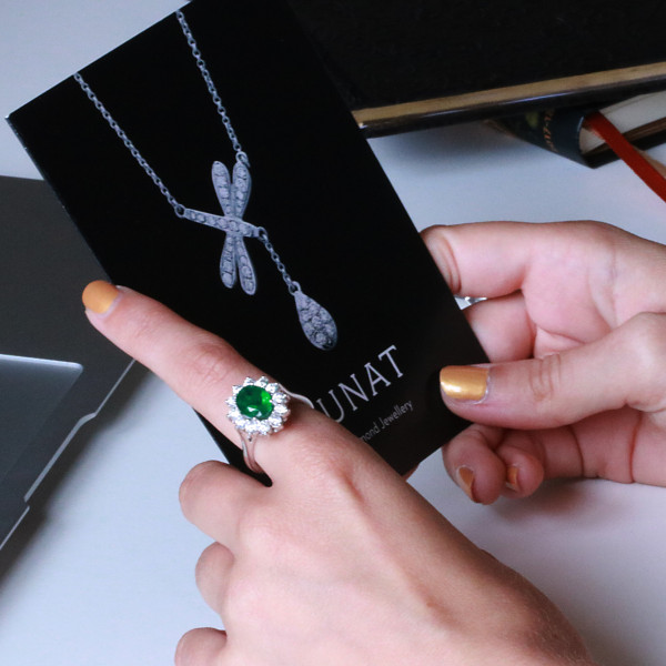 Woman wearing a halo ring with oval emerald on index finger, holding a package – BAUNAT - No description with photo
