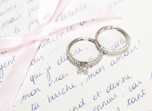 wedding ring and engagement ring resting on a letter, beautifully tied with a pink ribbon, symbolising love and commitment.