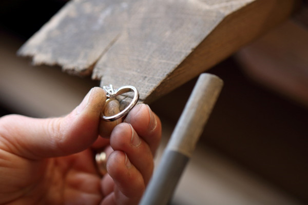 bir kuyumcu, bir yüzüğün metal bandını yeniden boyutlandırmaya odaklanarak bir makine üzerinde çalışmak için bir alet kullanır