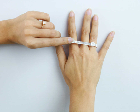 parmak ölçüsünü doğru bir şekilde ölçmek için yüzük boyutlandırma aleti kullanan bir kadın