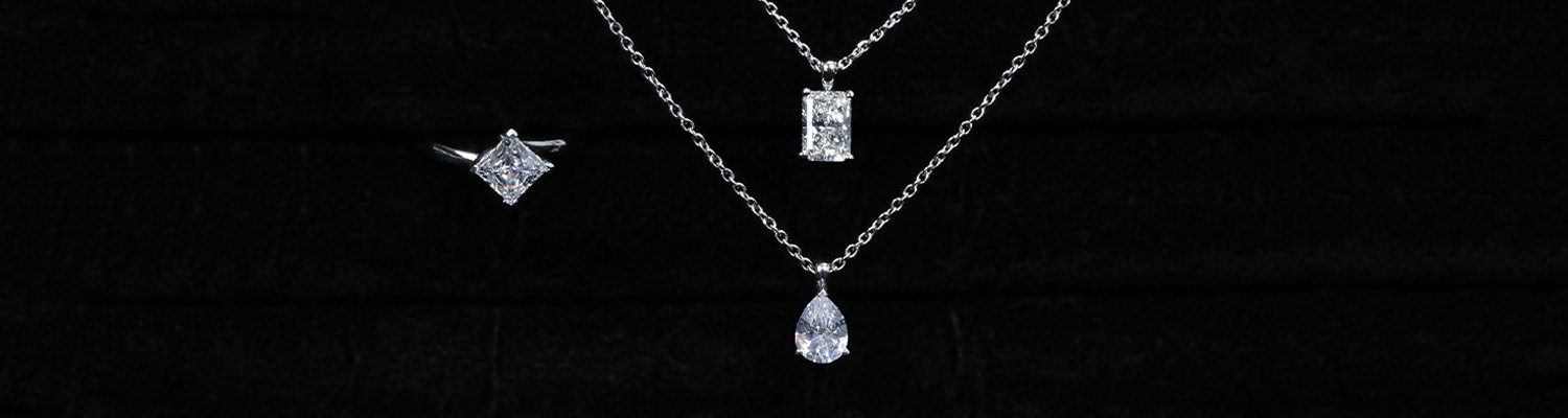 White gold diamond pendant necklace, rectangular and pear-shaped solitaire settings on black background