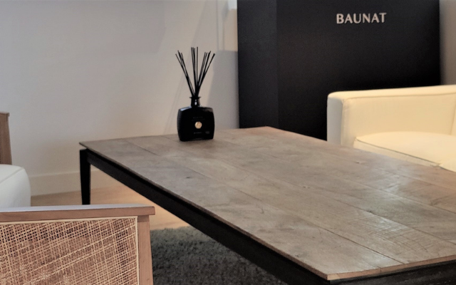 BAUNATロゴのあるモダンなラウンジ。白いソファと籐張りチェア、木製ローテーブルが並ぶ洗練された空間