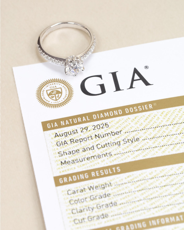 白金戒指鑲嵌圓形明亮式鑽石主石，戒圈旁排鑽設計，置於 GIA 鑽石證書文件上
