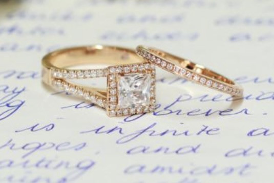 twee roodgouden ringen, één met een grote vierkante edelsteen en de andere met kleine ronde diamanten, geplaatst op handgeschreven cursieve tekst 