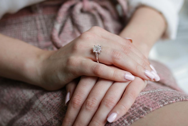 gouden verlovingsring met ronde diamant in solitaire zetting op hand met roze nagels