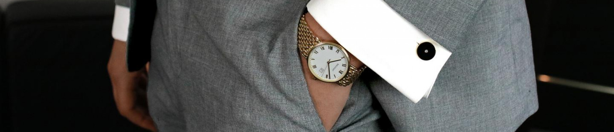 Gouden herenhorloge met witte wijzerplaat en meshband onder grijs maatpak