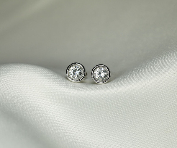 Twee ronde diamanten oorstekers in witgoud met bezelzetting, modern en minimalistisch