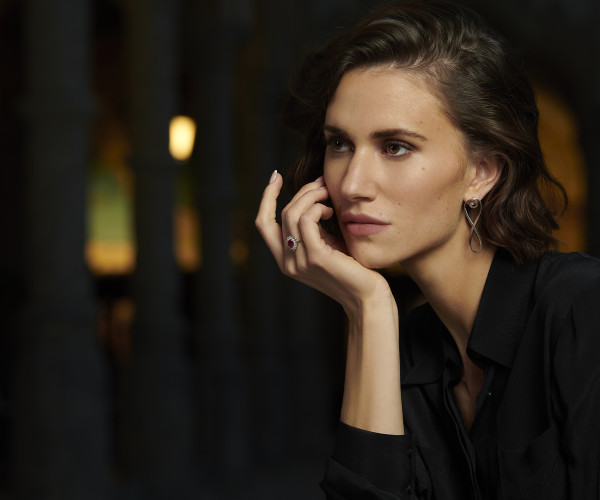 Vrouw met elegante wittegouden diamanten ring met rode edelsteen en verfijnde gouden oorhanger