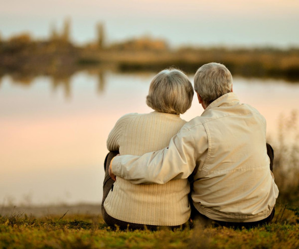 Een oudere man en vrouw ontspannen samen op het gras aan de oever van een rustig meer